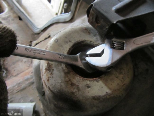 Процесс отворачивания гайки штока задней стойки рожковым и разводным ключами в ВАЗ-2110